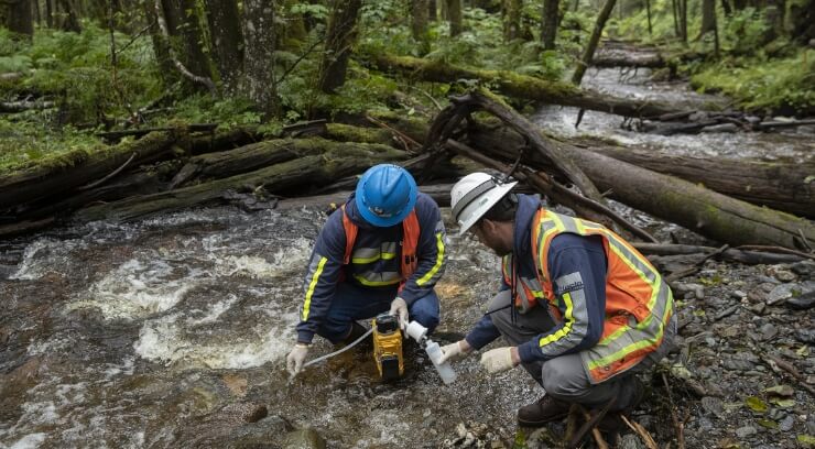 Two mining workers taking water samples from a stream